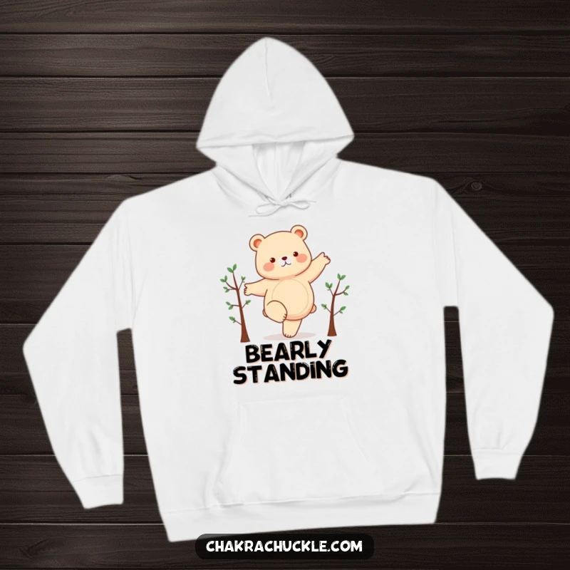 Funny hoodie featuring a chubby bear humorously attempting a yoga pose on one leg, arms extended like branches, radiating cozy amusement.